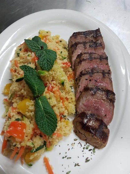 Gegrilltes Fleisch neben buntem Couscous-Salat mit Minze.