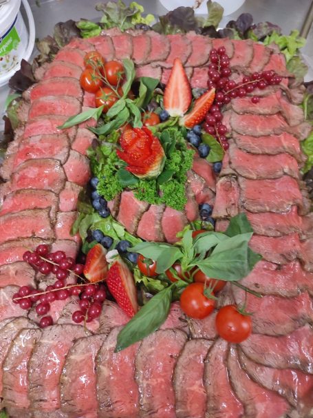 Dekorativ angerichtetes Fleisch mit frischen Beeren und Gemüse auf Salat.