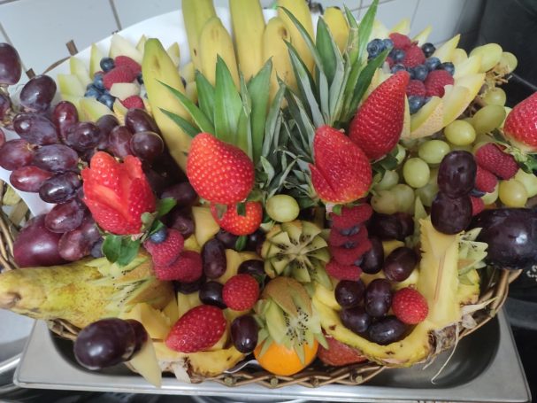 Bunte Obstschale mit Bananen, Trauben, Erdbeeren, Ananas und verschiedenen Beeren.