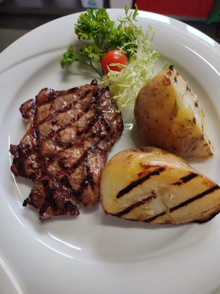 Gegrilltes Fleisch, Kartoffel, frischer Salat und Kirschtomate auf einem weißen Teller.