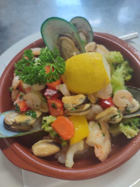 Meeresfrüchtesalat mit Garnelen, Muscheln, Gemüse und Zitronenscheibe auf einem Teller.