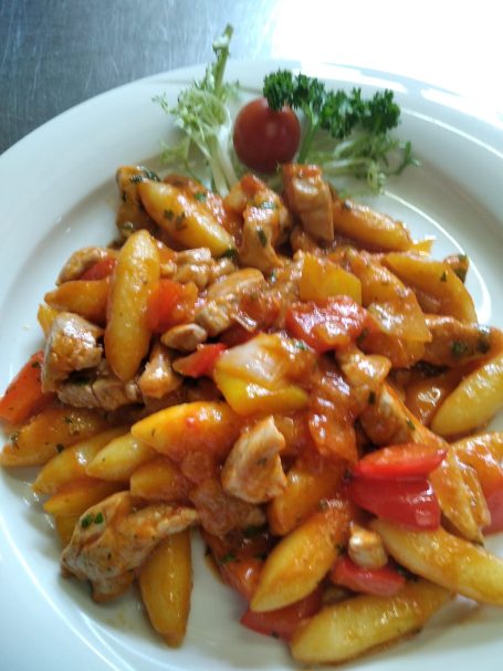 Pasta mit Fleischstücken, Tomatensauce und frischem Gemüse, garniert mit Salat und Kirschtomate.